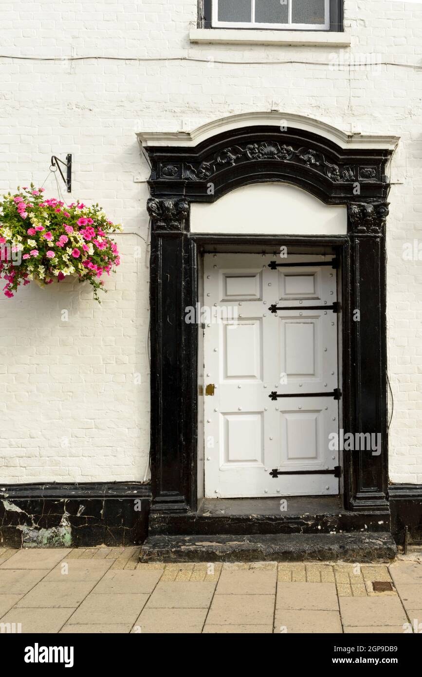 Porte classique blanche et noire sur façade en briques peintes blanches avec un seau de fleurs à proximité, tourné dans un village touristique sur la Tamise Banque D'Images