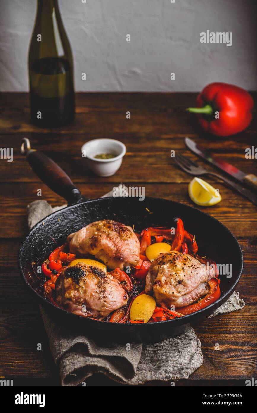 Cuisses de poulet cuites avec des poivrons rouges, du romarin et du citron dans une poêle en fonte. Banque D'Images