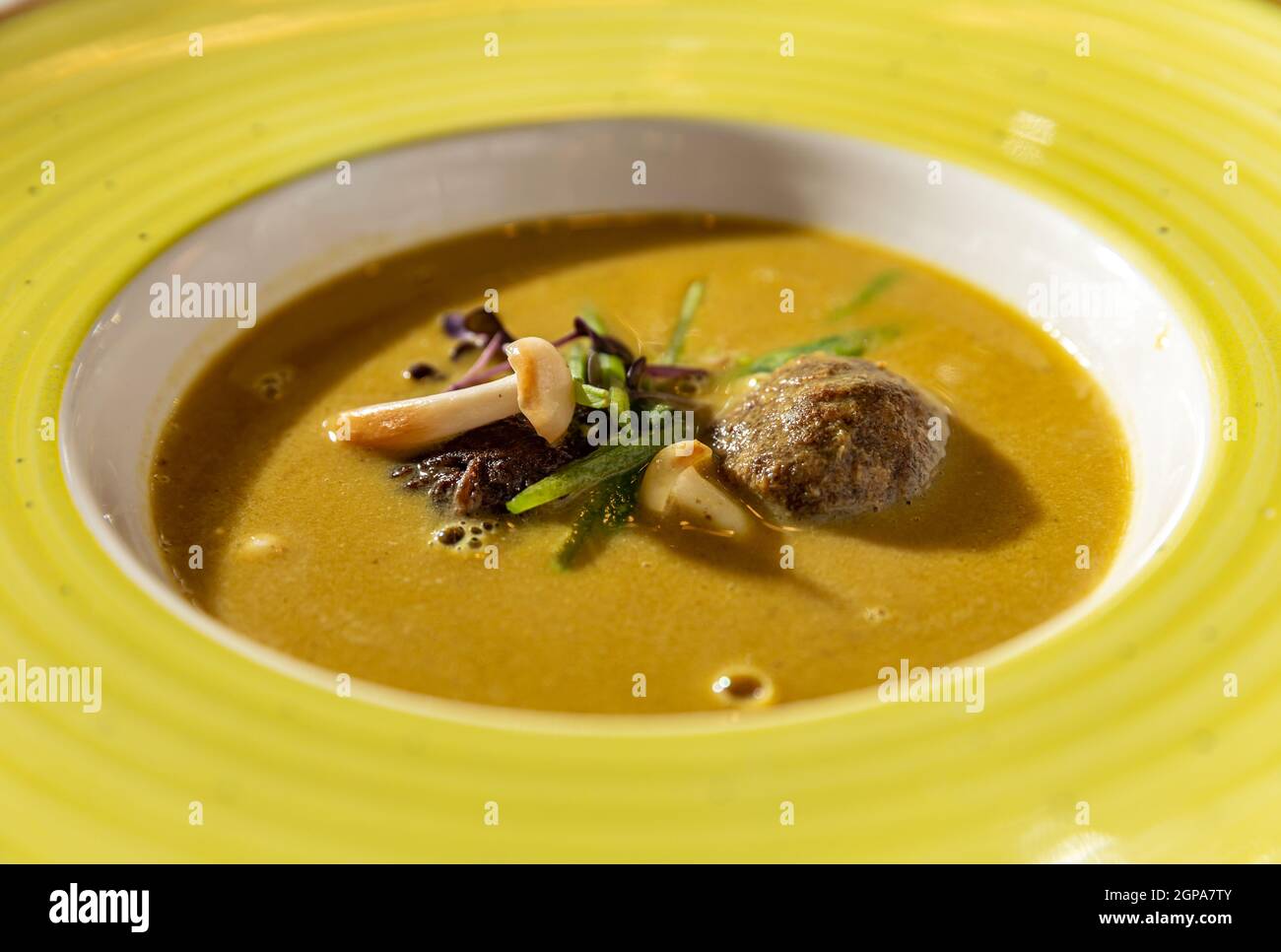 Gros plan de la soupe à la crème avec des boulettes de viande et des gousses de pois croquantes décorées de champignons enoki Banque D'Images