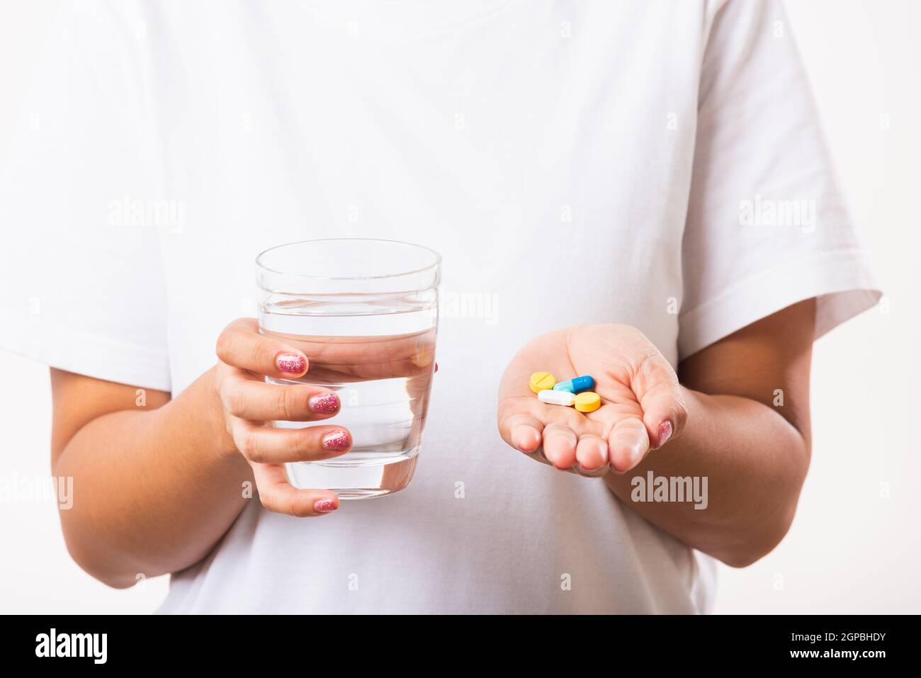Gros plan jeune femme asiatique tenir des médicaments à la main prendre des médicaments avec un verre d'eau, studio tourné isolé sur fond blanc, soins de santé et Banque D'Images