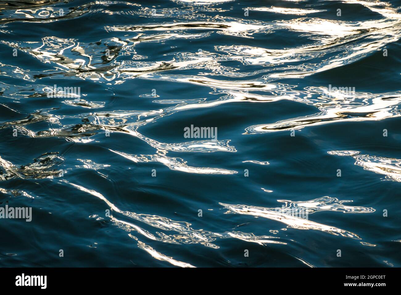 Arrière-plan de surface d'eau ondulé bleu foncé avec reflet de lumière du soleil dorée Banque D'Images