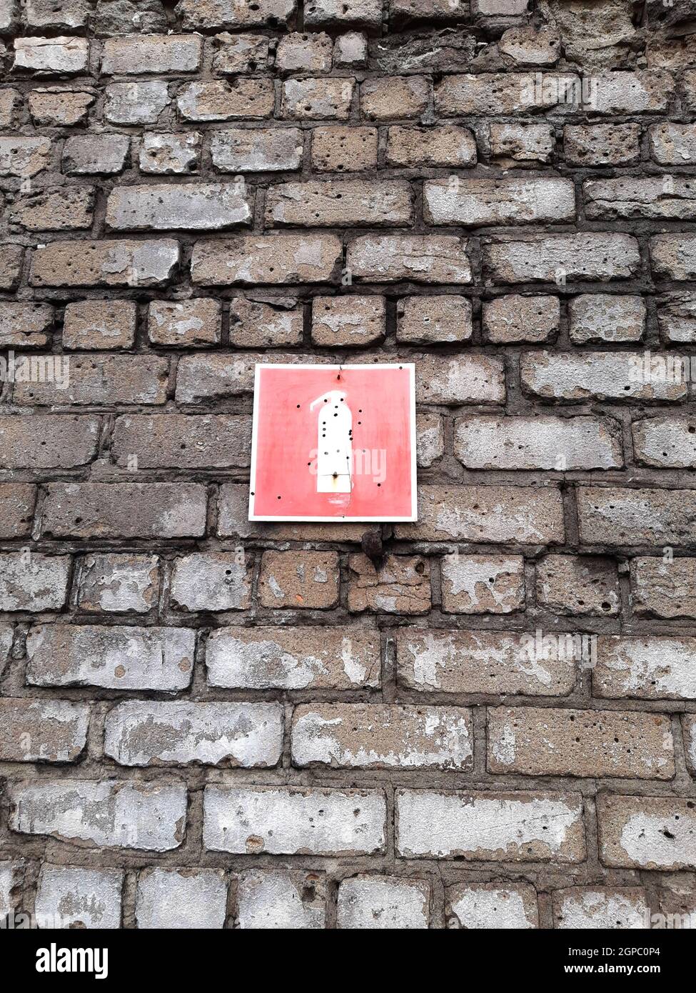 Panneau d'extincteur sur un mur de briques avec trous de balle rapprochés. Banque D'Images