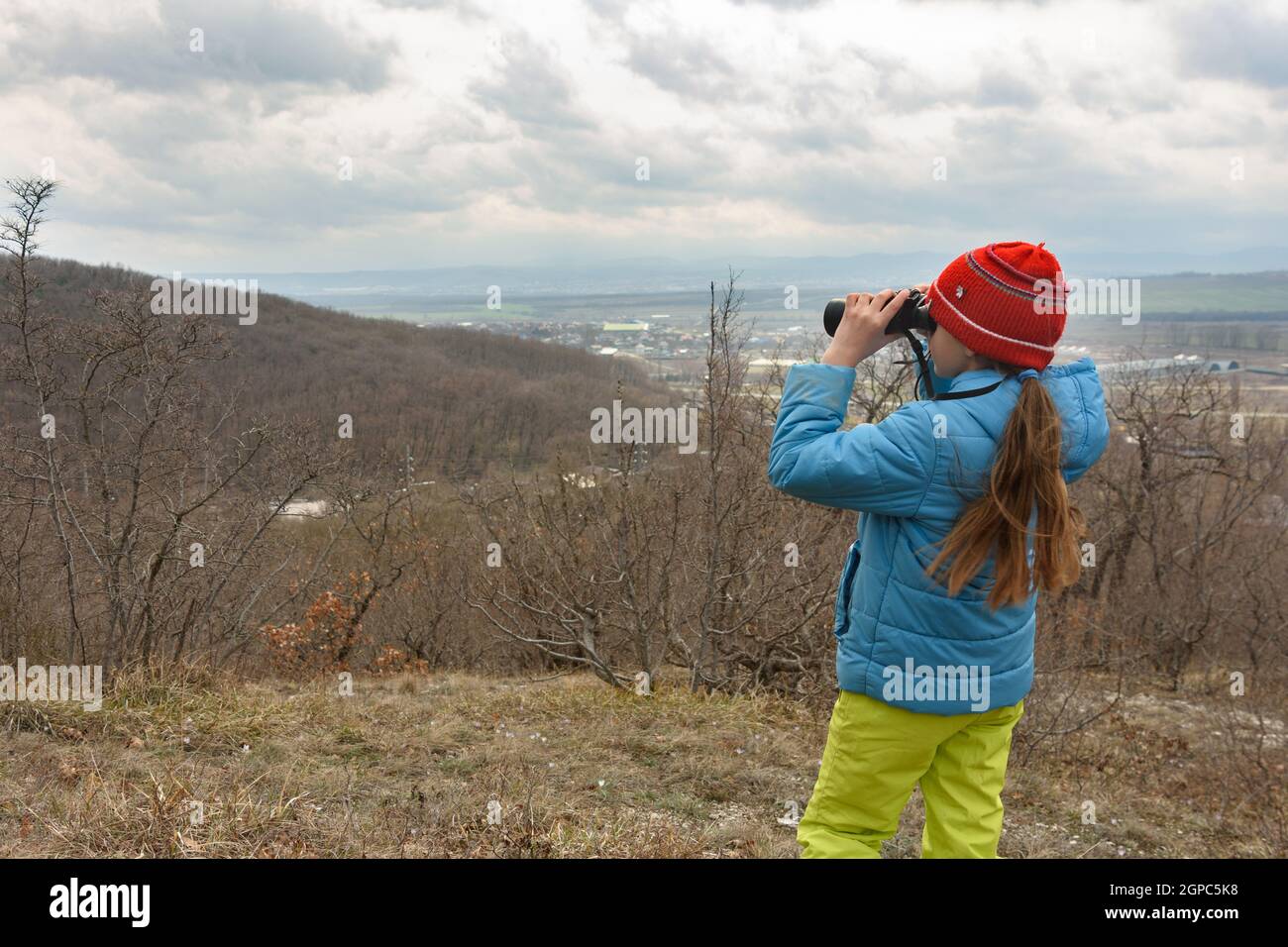 Une fille examine un paysage de montagne à travers des jumelles, vue de l'arrière Banque D'Images