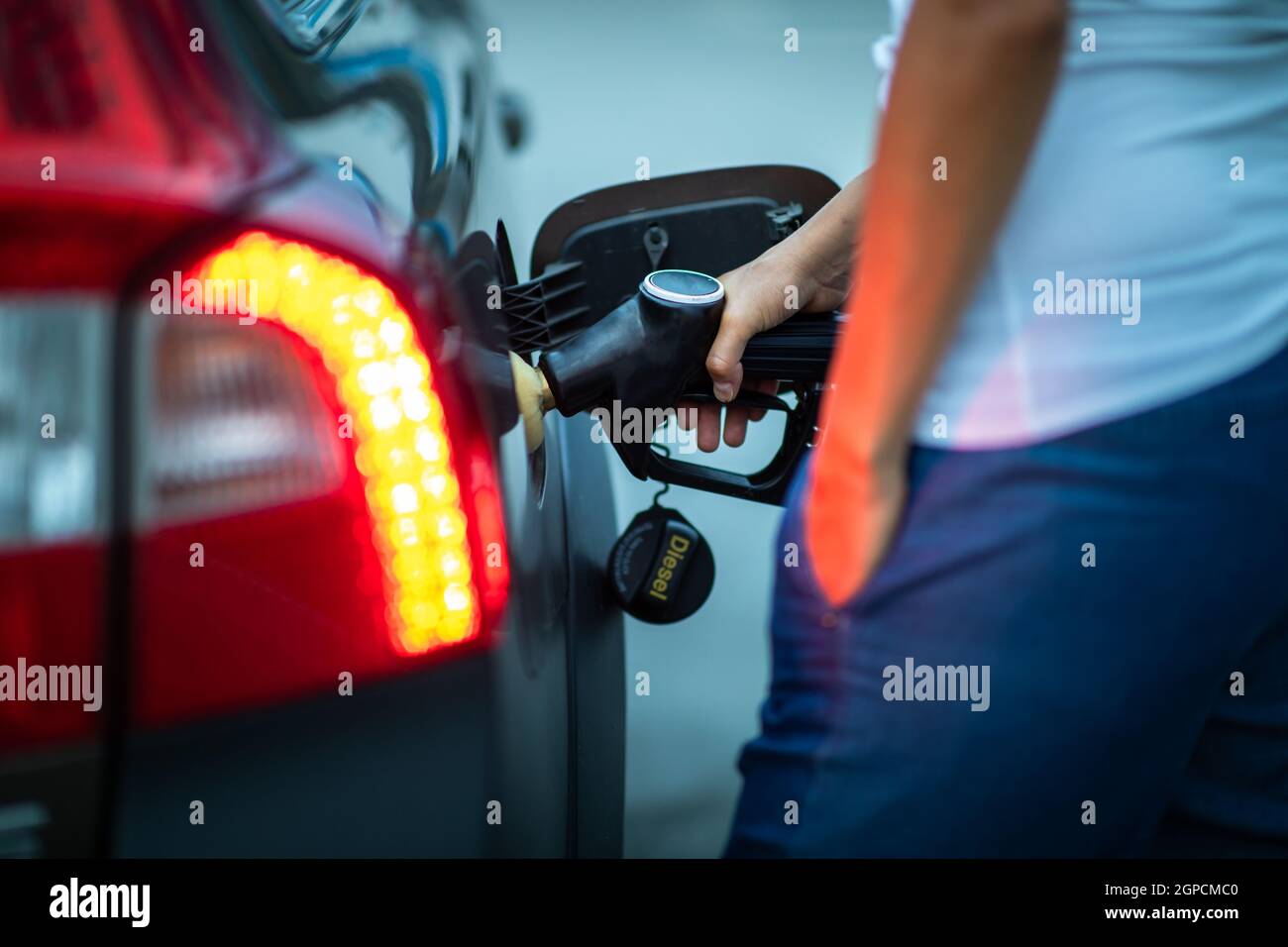 Jeune femme chauffeur ravitailler sa voiture la nuit avec du gaz (image colorée ; DOF peu profond) Banque D'Images