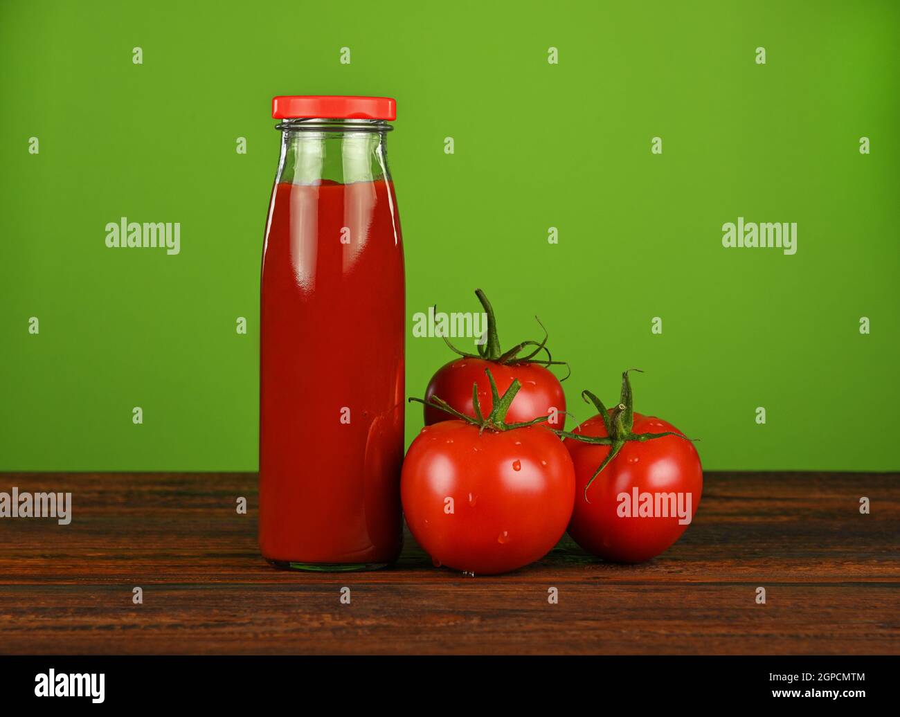 Fermez une bouteille en verre de sauce ketchup et de tomates rouges fraîches sur une table en bois sur fond vert avec espace pour les copies, vue à angle bas Banque D'Images