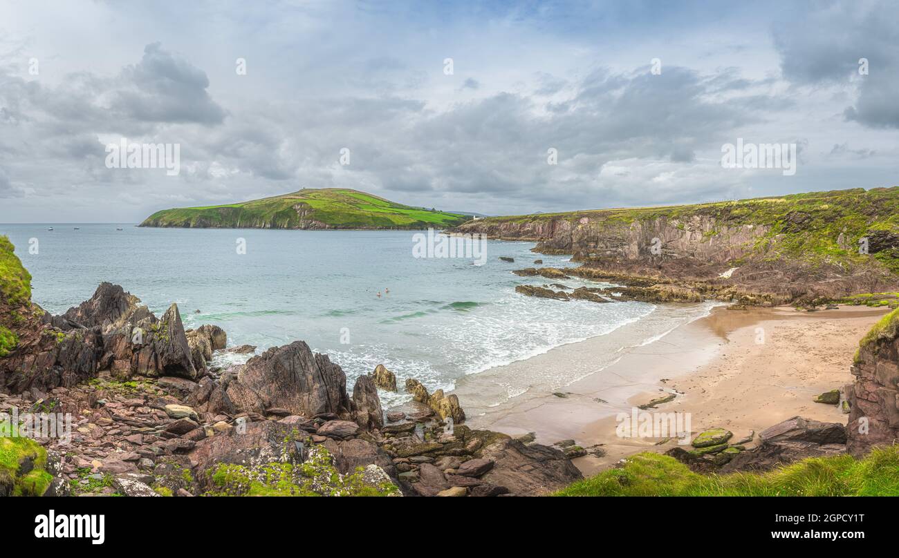 Dingle Lighthouse guide les bateaux de pêche de retour. Les personnes qui nagent dans l'eau froide de l'océan Atlantique. Plage cachée entre les falaises, Kerry, Irlande Banque D'Images