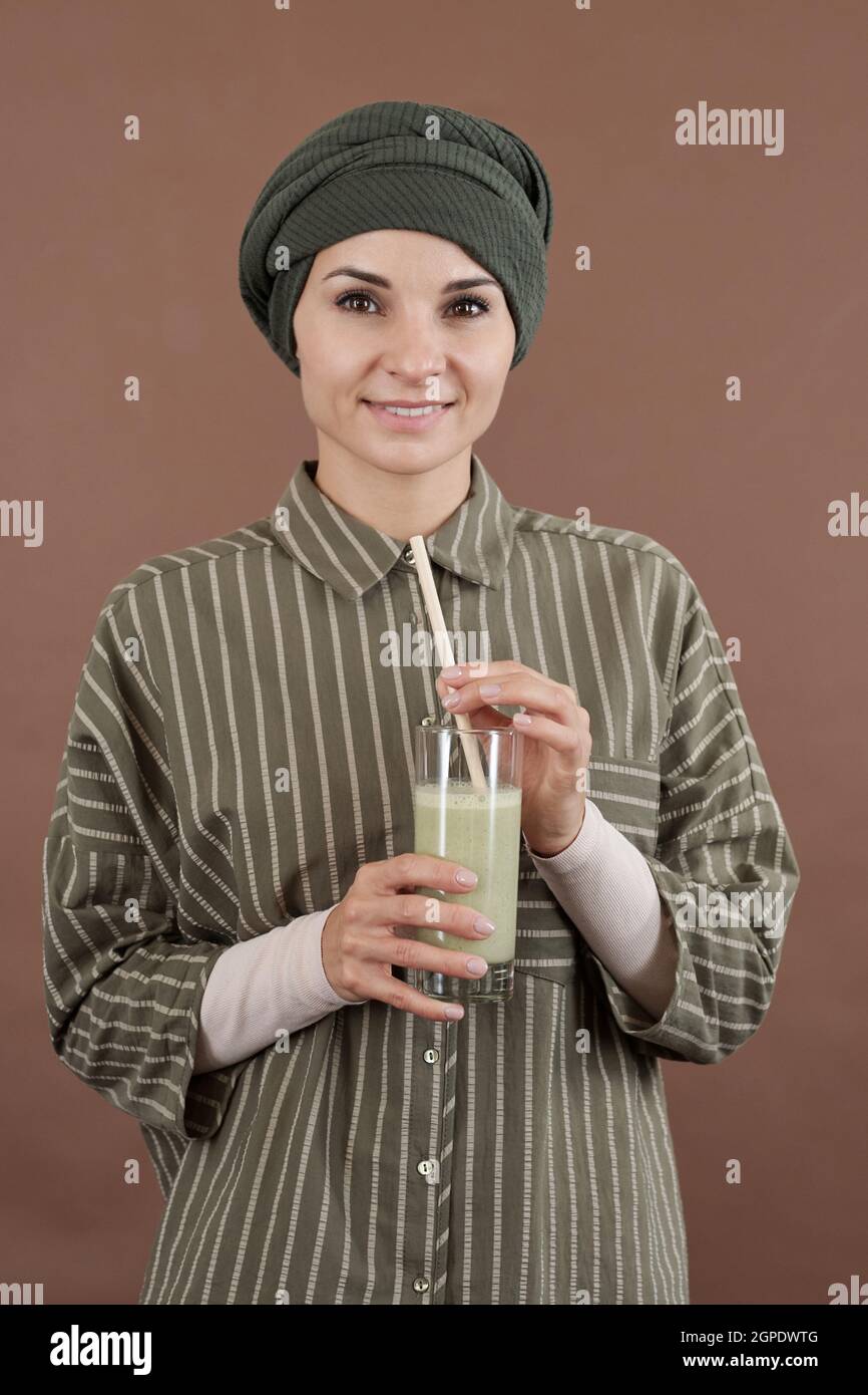Portrait en studio vertical moyen d'un musulman joyeux tenant un verre plein de délicieux smoothie boire sourire à l'appareil photo Banque D'Images