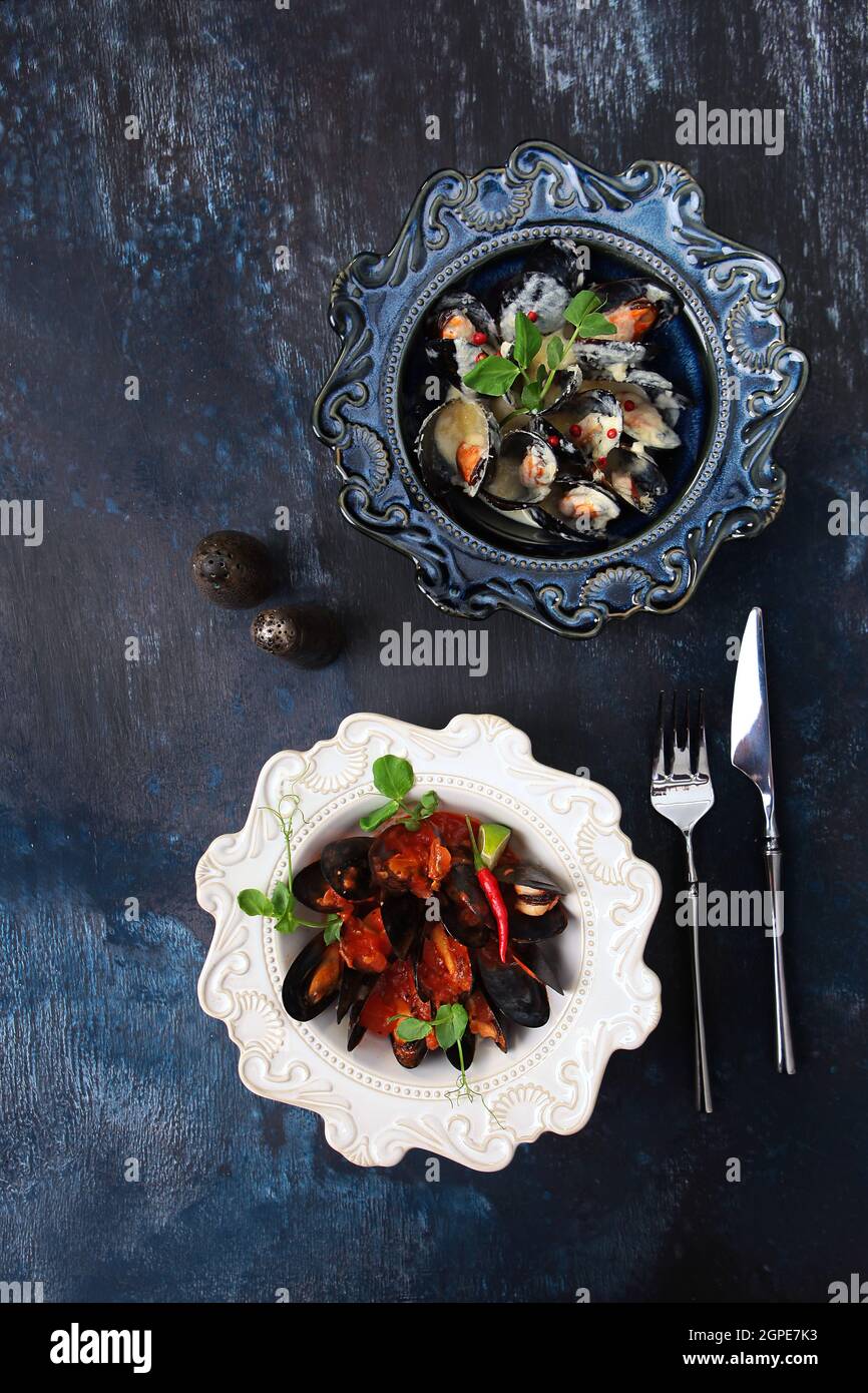 Moules en sauce crème. Moules dans une sauce tomate au poivre rouge chaud. Fruits de mer sur une assiette. Deux plats en céramique élégante. Vue de dessus. Texturé bleu Banque D'Images