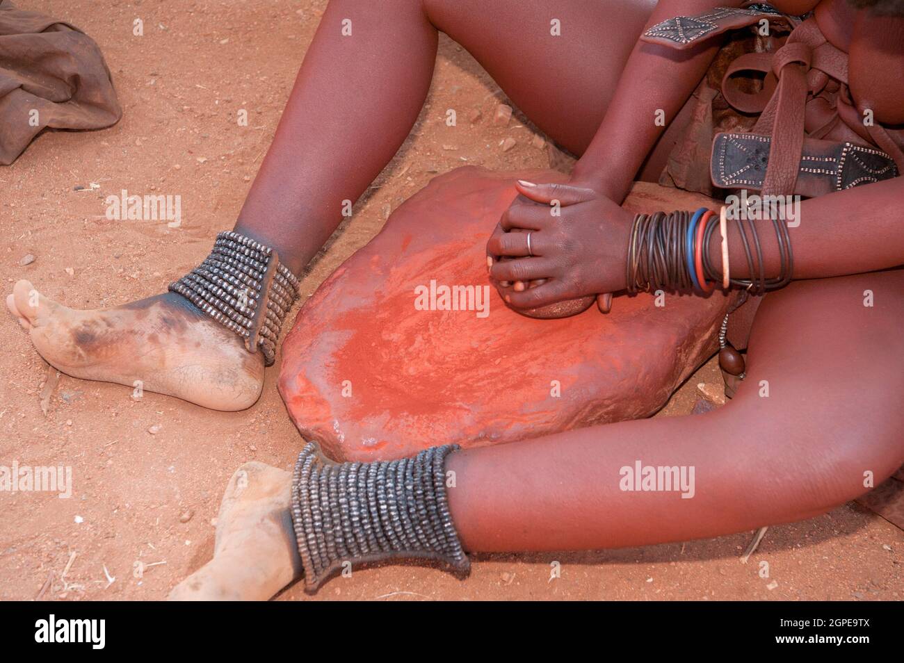 Femme Himba écrase d'argile rouge, c'est ensuite utilisé pour enduire leurs cheveux. Photographié dans un village Himba, Epupa Falls, Kaokoland, Namibie, Afrique Banque D'Images