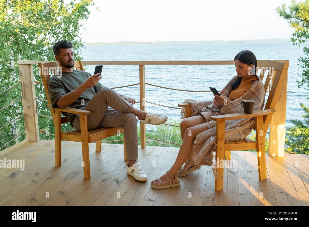 Jeune mari et femme avec un smartphone se reposant au bord de la mer pendant les vacances d'été Banque D'Images