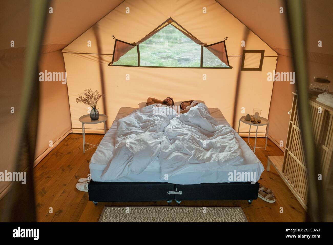 Jeune couple fatigué dormant sur un grand lit double sous des draps blancs  dans une tente de glamping Photo Stock - Alamy