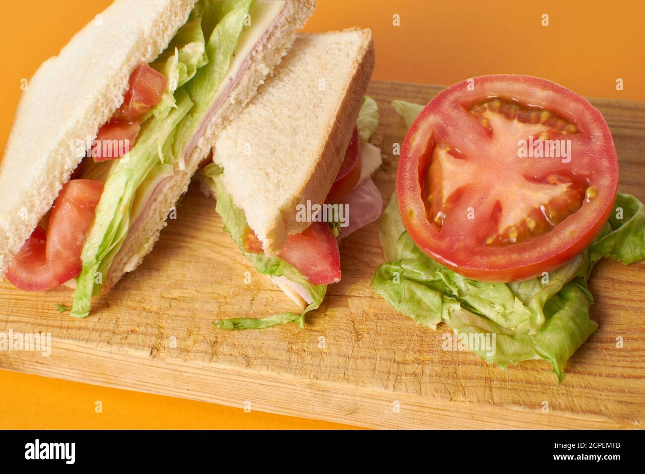 Sandwich sain au jambon et au fromage avec tomate et laitue sur fond orange Banque D'Images