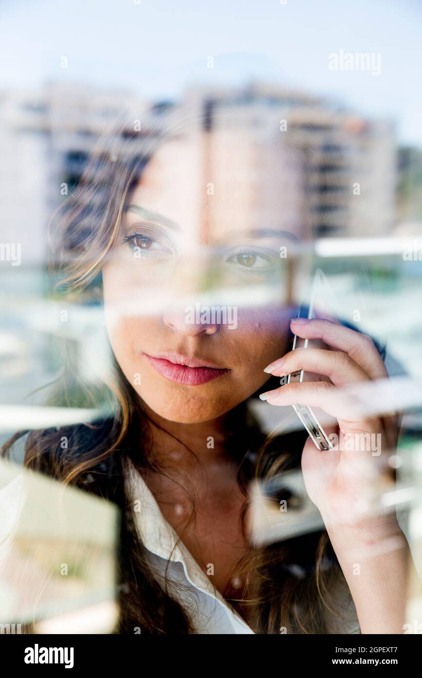 Une jeune femme d'affaires frustrée se reflète dans la fenêtre de son bureau lorsqu'elle parle sur un téléphone mobile Banque D'Images