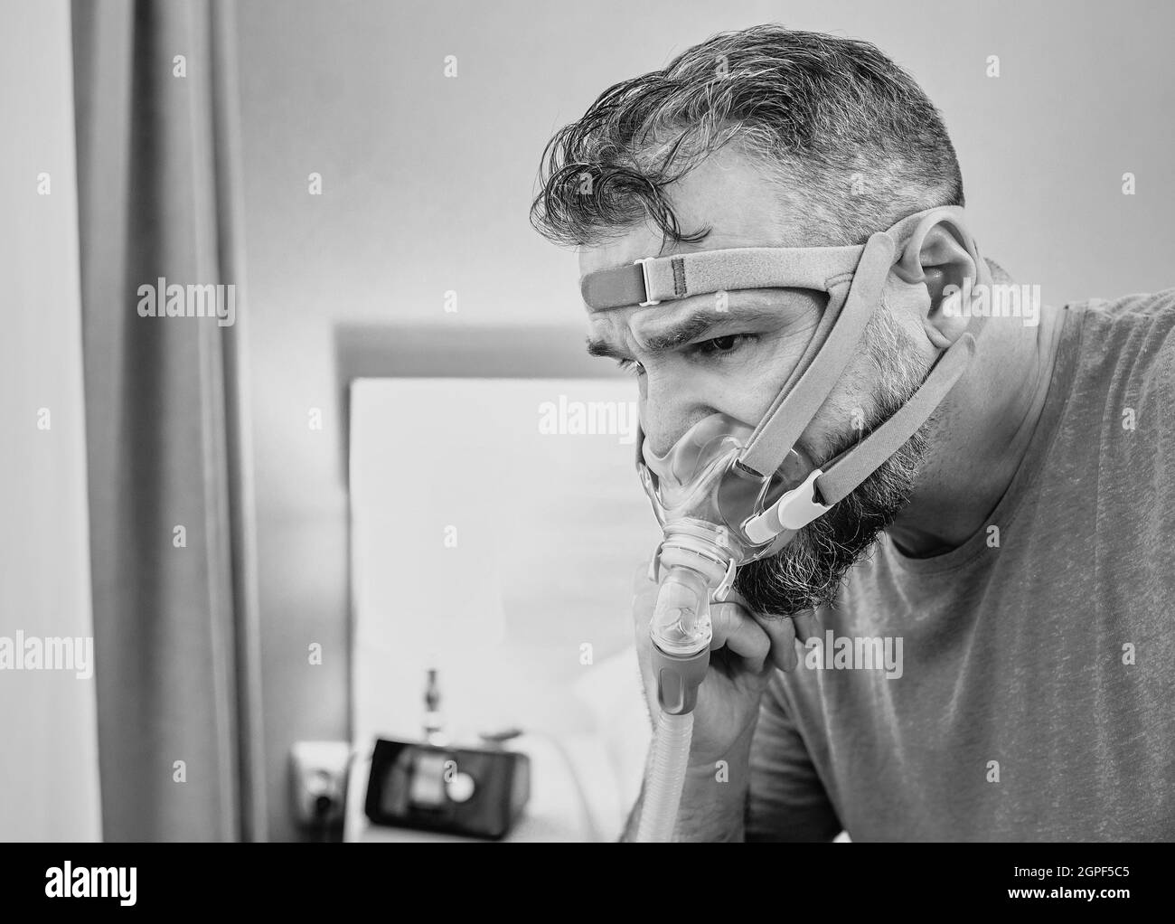 Malheureux homme choqué avec des problèmes respiratoires chroniques surpris par l'utilisation de la machine de PPC assis sur le lit dans la chambre à coucher. Banque D'Images