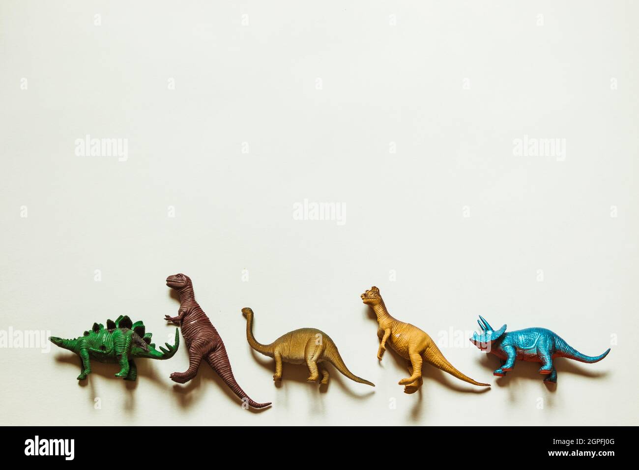 Cinq dinosaures en peluche se trouvent dans une rangée sur un fond blanc. Banque D'Images