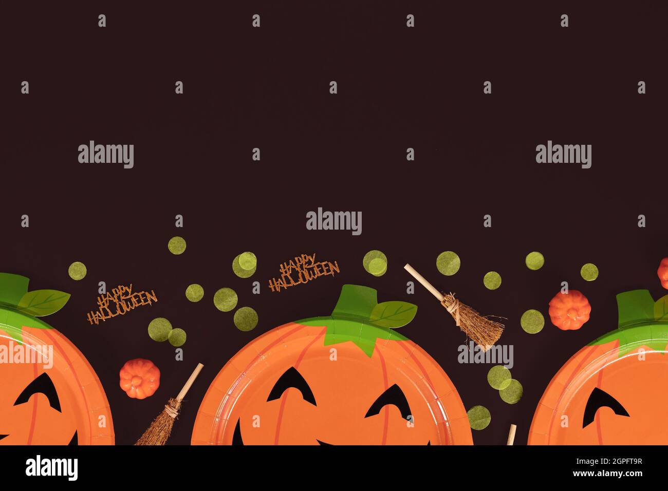 Assiettes en papier de citrouille orange Halloween, balais de sorcière, confetti et texte joyeux Halloween en bas de fond noir avec espace pour les copies Banque D'Images