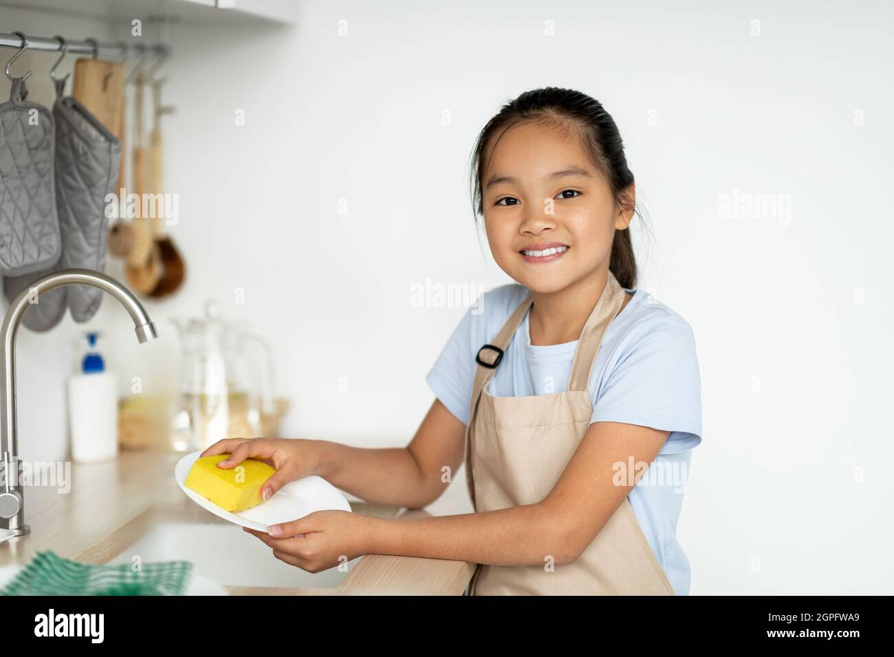 Petite gouvernante. Bonne fille asiatique aidant la mère dans la cuisine, laver et essuyer la vaisselle, debout dans la cuisine Banque D'Images