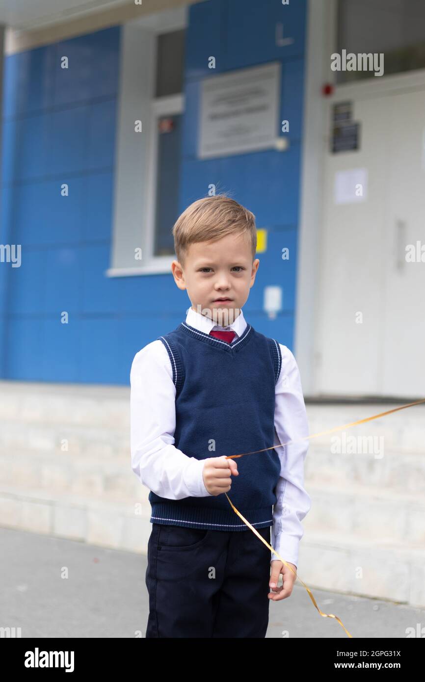 Jeune garçon de première année à l'école avec un ballon dans la main le jour d'automne ensoleillé. Célébration le 1er septembre. Journée des connaissances. Mise au point sélective Banque D'Images