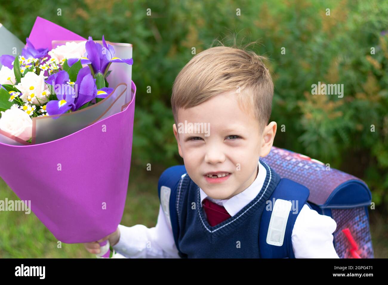 Un adorable jeune garçon de première année dans un uniforme d'école avec un beau bouquet de fleurs colorées dans la cour d'école après les vacances du 1er septembre. Connaissance Banque D'Images