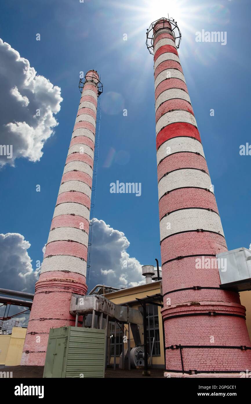 Cheminées d'usines industrielles. Extérieur de l'installation de chauffage urbain avec cheminées industrielles contre le soleil et le ciel bleu. Vue à angle bas. Banque D'Images