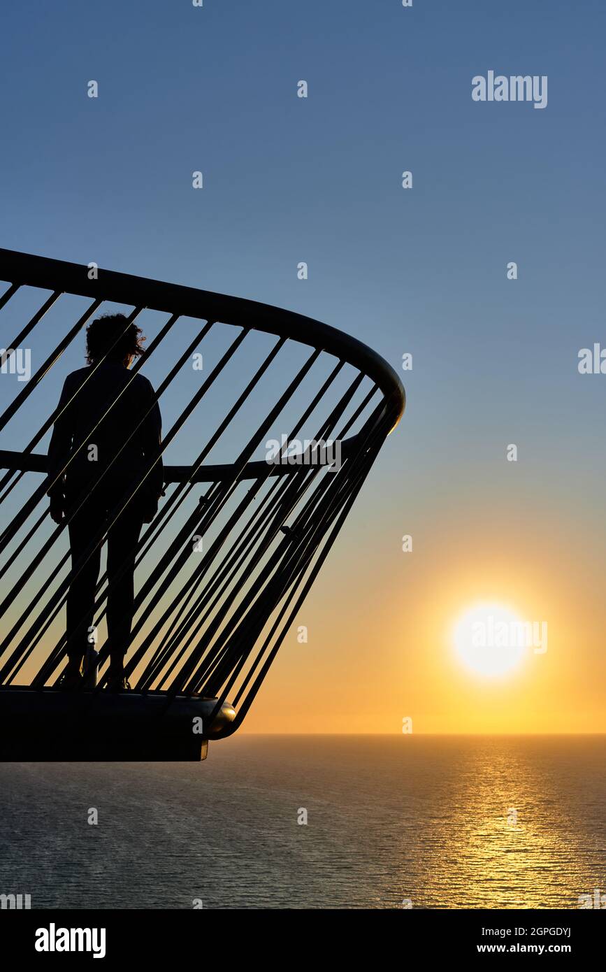 Femme sur un pont regardant un lever de soleil sur la mer Banque D'Images