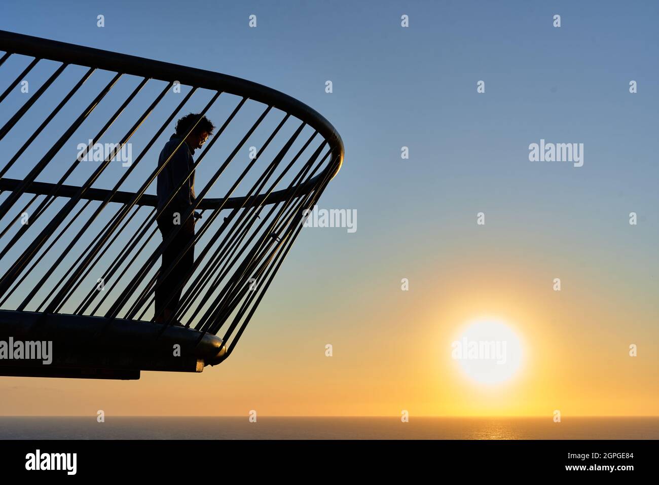Femme sur un pont regardant un lever de soleil sur la mer Banque D'Images