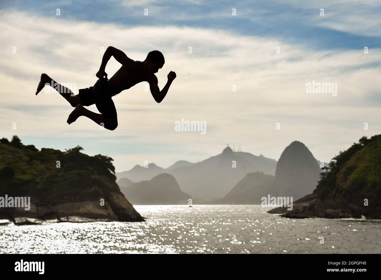 Silhouette d'un Buy saut dans l'océan avec la montagne de Sugarloaf et Corcovado sur fond, à Niteroi, Rio de Janeiro, Brésil Banque D'Images