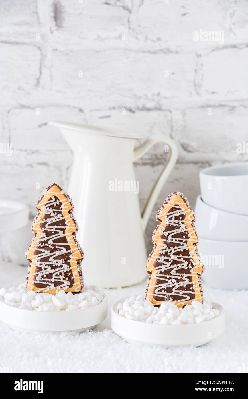 Deux biscuits en forme d'arbres de noël avec glaçage au chocolat et au sucre dans des bols avec du sucre grossier sur fond blanc, vertical avec espace de copie Banque D'Images