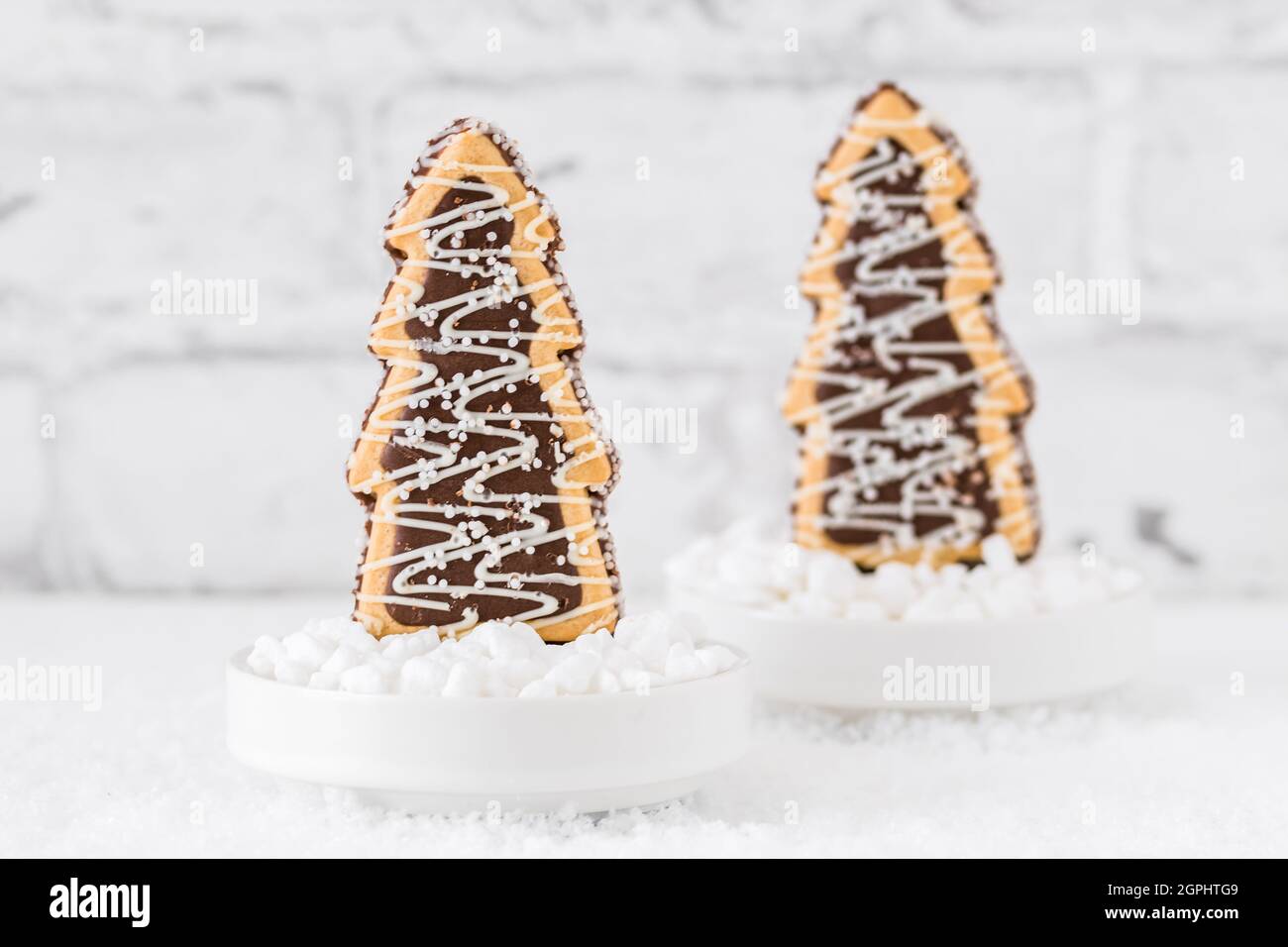 Deux biscuits en forme d'arbres de noël avec glaçage au chocolat et au sucre dans des bols avec du sucre grossier sur fond blanc Banque D'Images