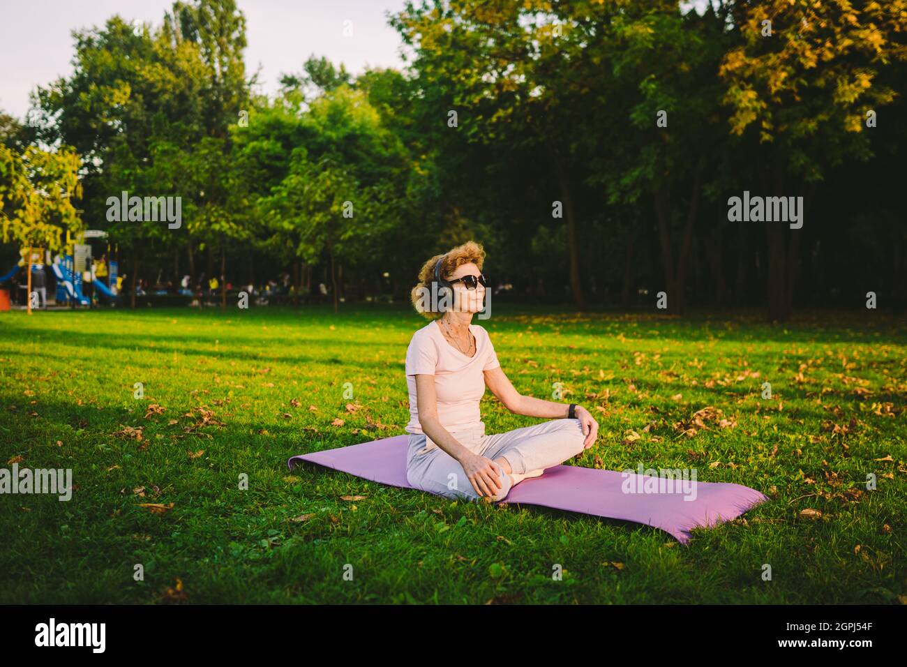 Yoga au parc. Une femme d'âge moyen dans le lotus pose assis sur un tapis de yoga sur l'herbe verte. Concept de calme et de méditation. Yoga à l'extérieur. Femme senior meditatin Banque D'Images