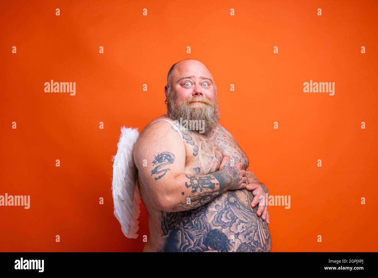 Gros homme peur avec la barbe, tatouages et ailes agit comme un ange Banque D'Images