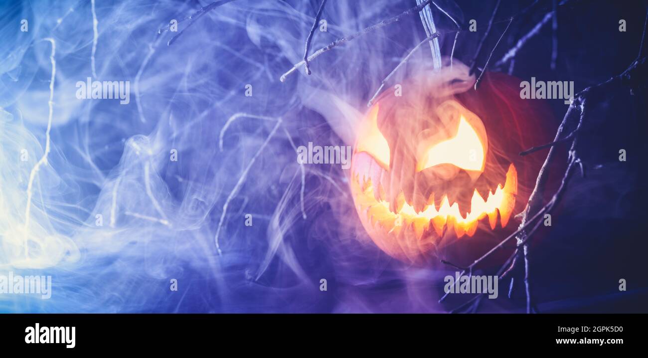 Citrouille de citrouille d'Halloween effrayante et sculptée avec un visage effrayant qui brille et qui émet de la fumée la nuit. Banque D'Images