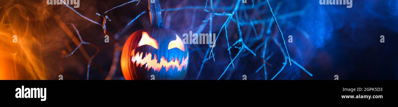 Citrouille de citrouille d'Halloween effrayante et sculptée avec un visage effrayant qui brille et qui émet de la fumée la nuit. Banque D'Images