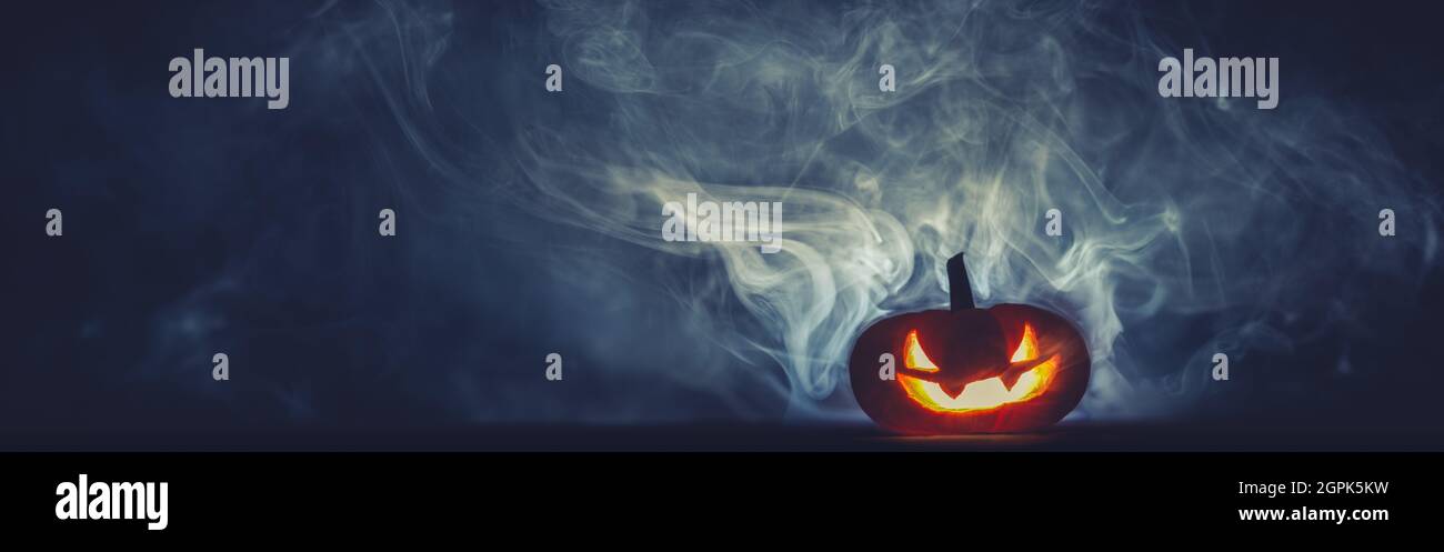 Jack o Lantern sombre et sculpté rouge éclatant dans une fumée épaisse la nuit. Arrière-plan Halloween avec espace de copie pour le texte. Banque D'Images