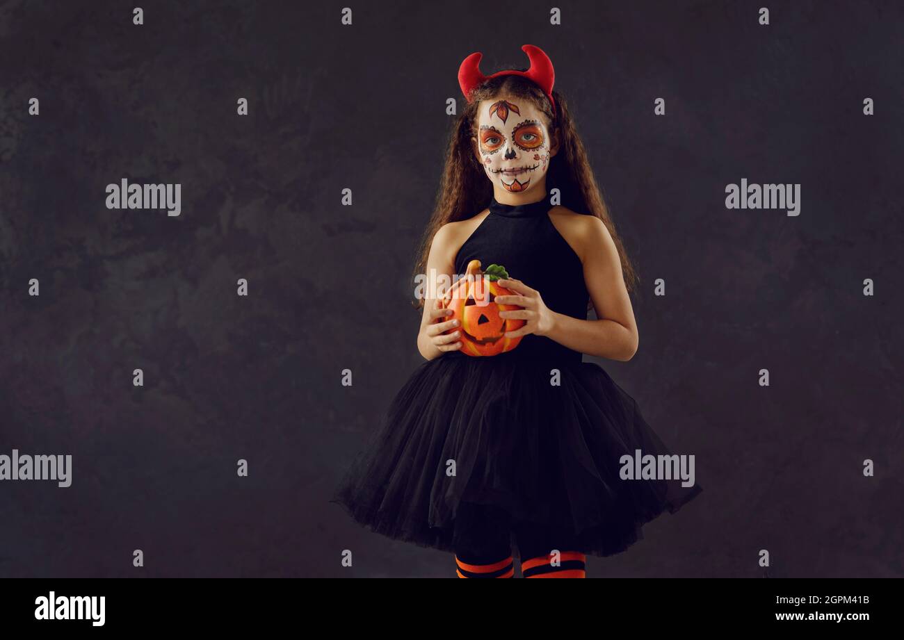 Portrait studio d'une petite fille avec un maquillage de crâne tenant une citrouille d'Halloween Banque D'Images