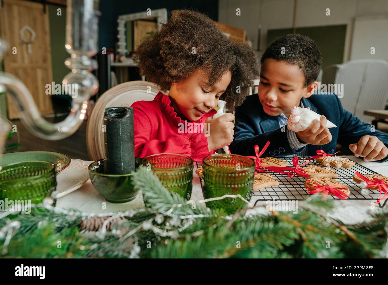Soeur et frère décorant des pains d'épices avec des rubans assis à la table à la maison. Concept de loisirs en famille pour Noël. Idée pour le bricolage fait main Hap Banque D'Images