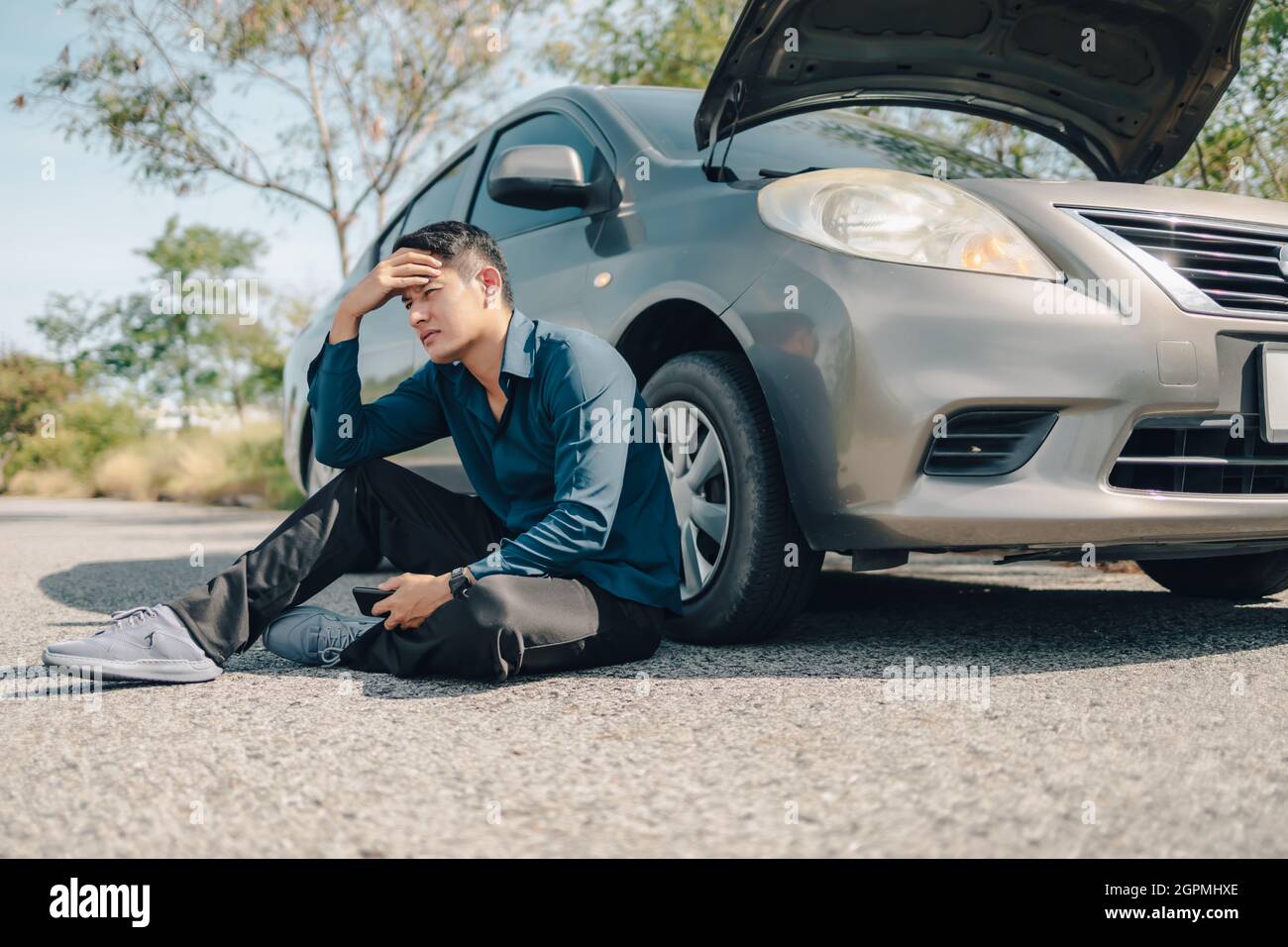 Homme sérieux mal de tête assis à côté d'une voiture en panne sur la route. Concept de voiture brisée. Banque D'Images
