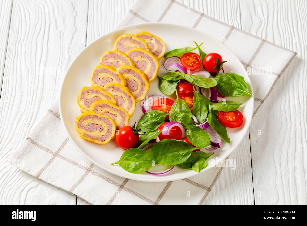 jambon et fromage hachés petits-déjeuners omelettes, pignons et salade d'oignons rouges aux tomates fraîches aux épinards sur une assiette sur une table en bois blanc, horizontale v Banque D'Images