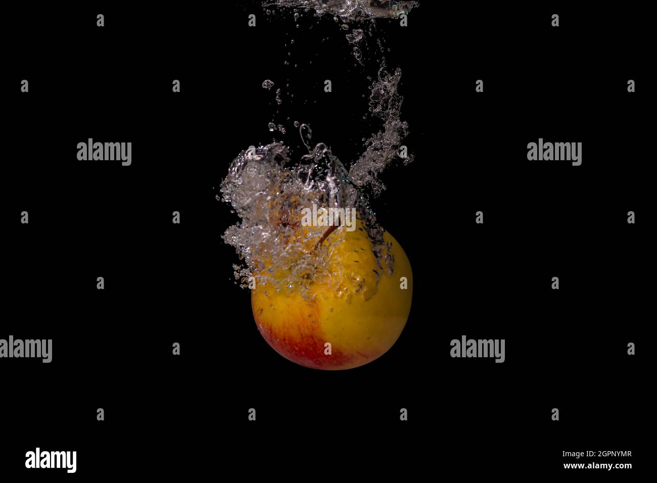 Les fruits frais tombent dans l'eau froide avec des bulles d'air comme symbole pour un style de vie végétalien sain dans une exposition courte durée de l'appareil photo haute vitesse Banque D'Images