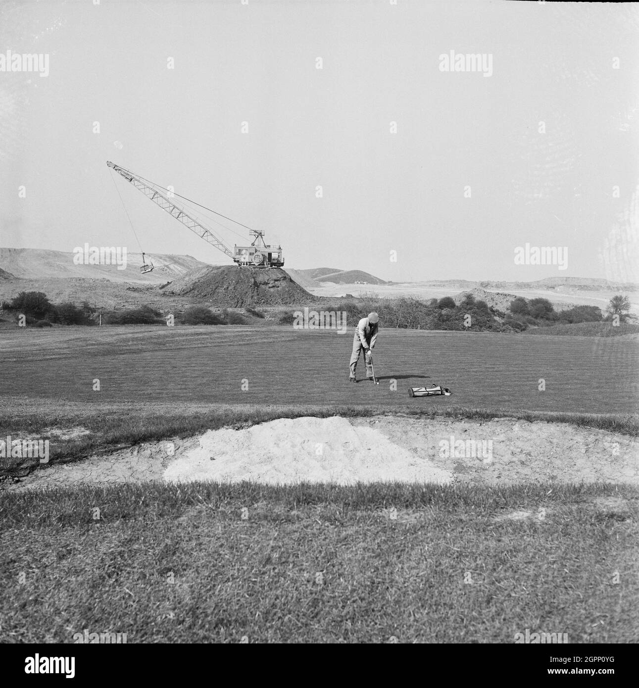 Une vue sur la restauration du parcours de golf de Whitley Bay après l'achèvement de l'exploitation minière en opencast sur le site, montrant un homme jouant au golf au premier plan et une grue sur une hanche de déblais en arrière-plan. John Laing and son Ltd a lancé des opérations d'exploitation minière en 1942 pour répondre aux besoins de la guerre. Le travail a été élargi par la compagnie après la guerre et, en 1948, l'exploitation minière de charbon opencast a eu lieu au terrain de golf du site de charbon Opencast, dans la région de Monkseaton, dans la baie Whitley. En 1953, la mine a été fermée et la terre a été récupérée. Banque D'Images