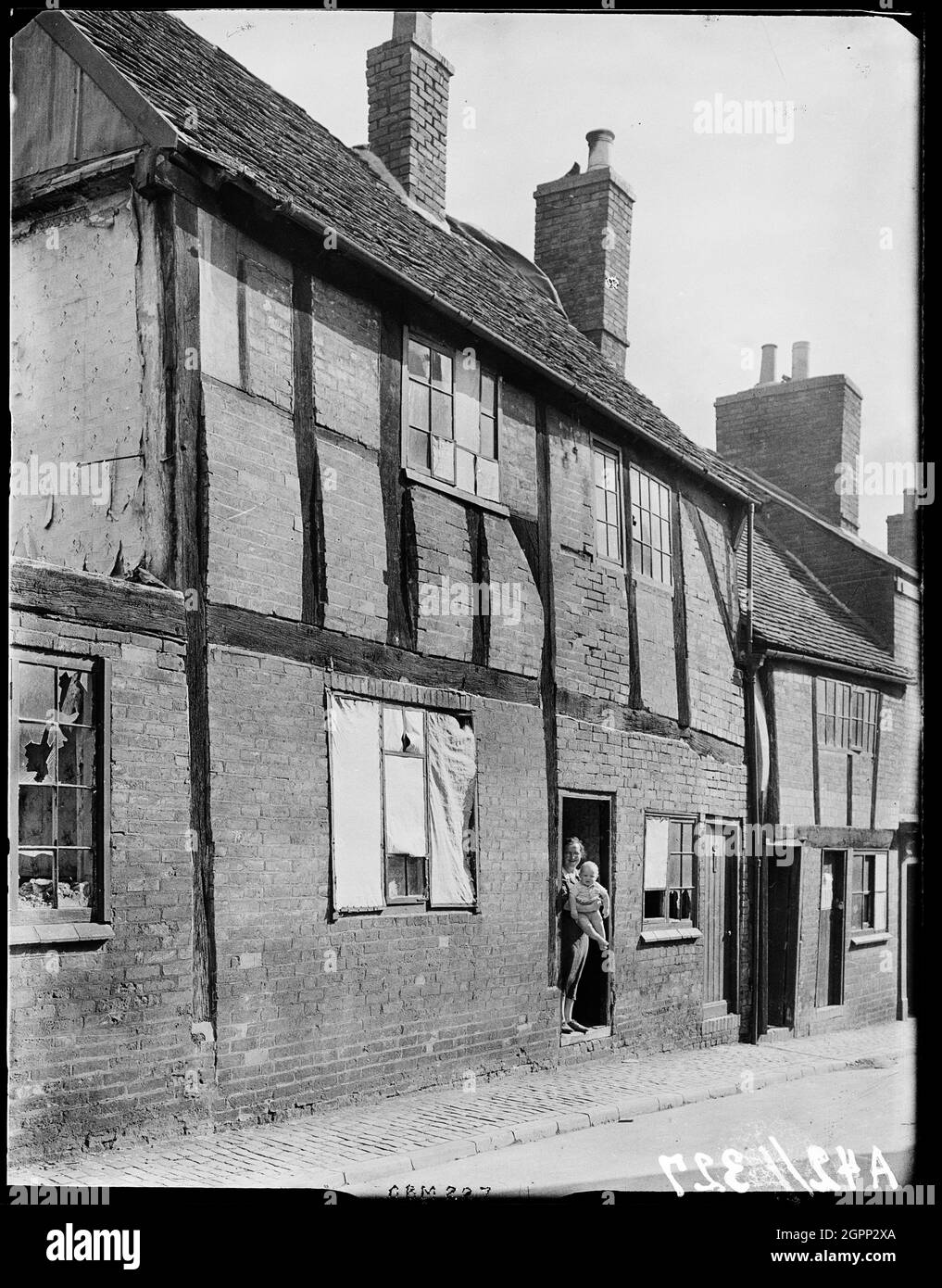 Nouvelle rue, Coventry, 1941. L'extérieur du 30 New Street avec une femme debout dans la porte de la maison tenant un bébé et les fenêtres sont montés à la suite de la bombe damageA note sous la photo rapporte que le bébé était "né pendant le grand RAID aérien". Le centre-ville de Coventry a été dévasté par des raids aériens en novembre 1940. L'attentat a laissé la cathédrale voisine en ruines et détruit une grande partie du tissu historique de la ville. La rue New a été démolie après la fin de la guerre. Banque D'Images