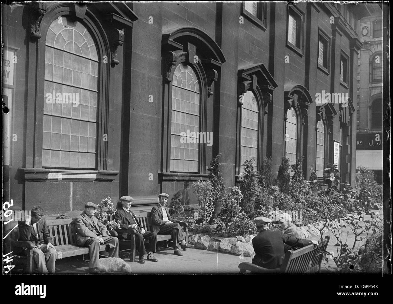 Église Sainte-Trinité, Boar Lane, Leeds, 1941. Vue extérieure de l'église de la Sainte Trinité, montrant le front sud avec des hommes assis sur des bancs au premier plan. L'église a été construite entre 1721 et 1727 par William Etty. La tour supérieure a été ajoutée après 1839 par R. D. Chantrell. Il a un plan rectangulaire avec sept par trois baies, avec une tour dans la baie centrale de l'extrémité ouest. Le front sud a une porte dans la première baie, des fenêtres avec des pediments triangulaires et segmentaires alternés au rez-de-chaussée, et un deuxième niveau au-dessus. Banque D'Images