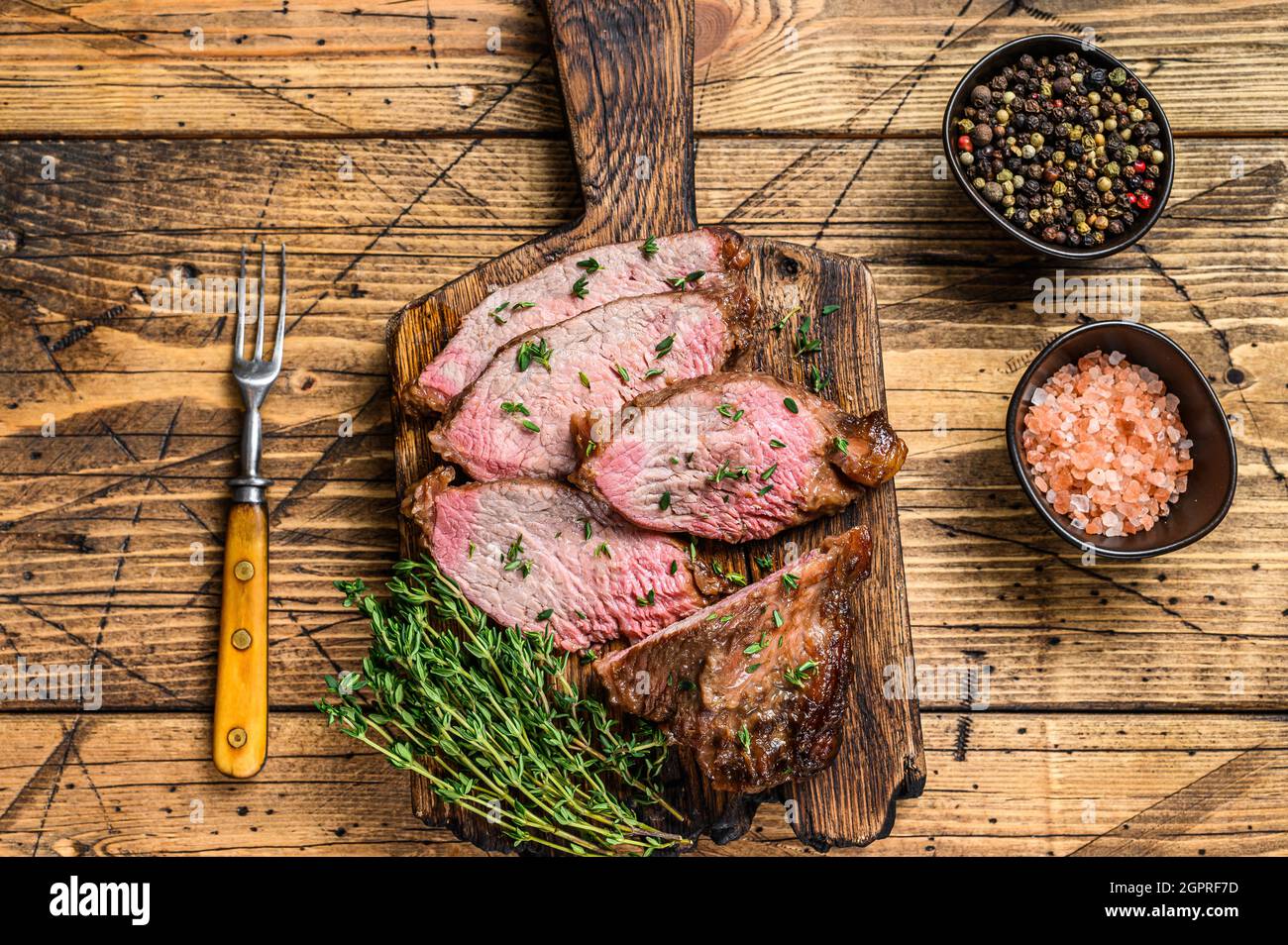 Tranches rares de rôti de boeuf sirloin à trois pointes steak bbq sur une planche à découper en bois. fond en bois. Vue de dessus Banque D'Images