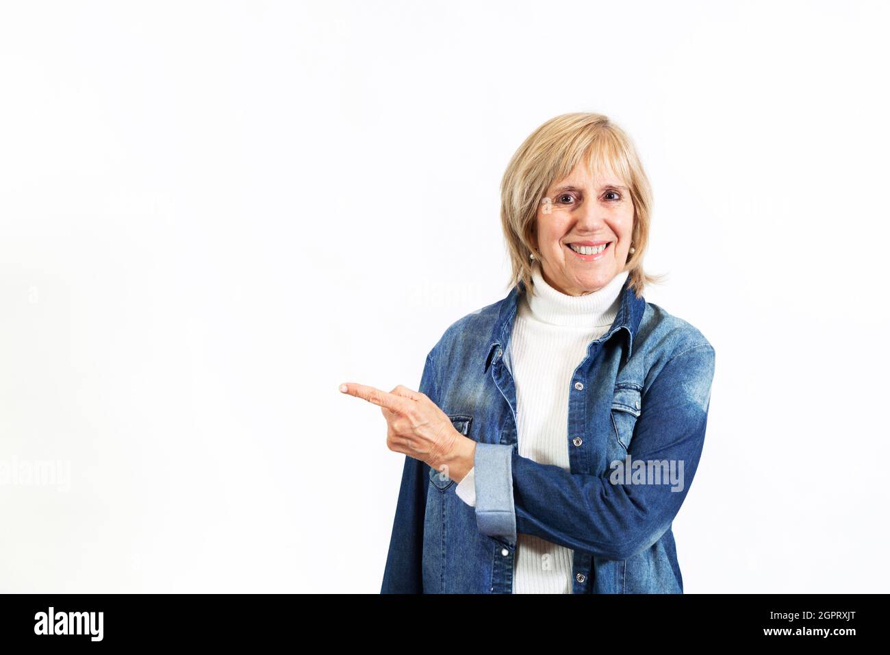Femme mûre souriante sur fond blanc pointant avec sa main. Image pour toile de fond ou maquette. Copier l'espace. Banque D'Images