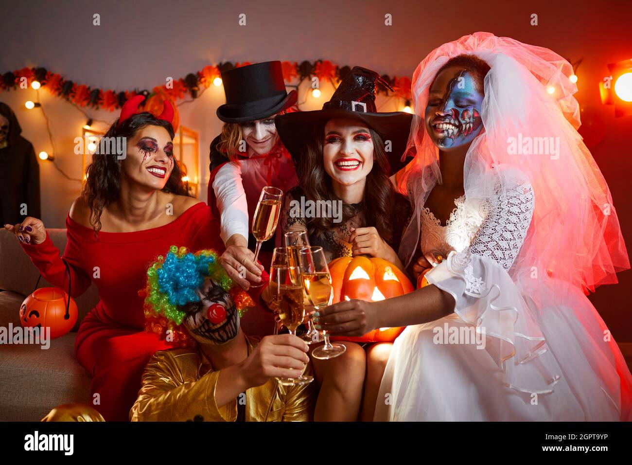 Groupe diversifié de jeunes amis heureux qui boivent et s'amusent à une fête d'Halloween Banque D'Images