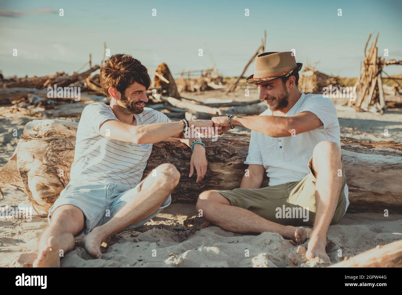 Deux garçons assis sur la plage se saluent les uns les autres avec leurs poings. Les jeunes ont fait des martelant leurs poings pour se saluer Banque D'Images