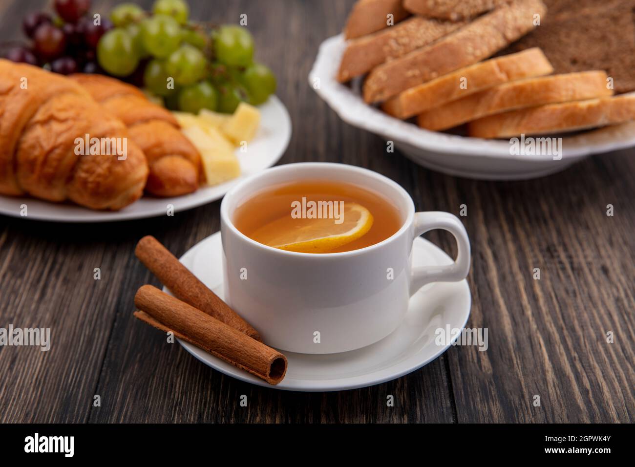 vue latérale d'une tasse de toddy chaud avec cannelle sur soucoupe et croissants avec tranches de raisin et de fromage et pains dans des assiettes sur fond de bois Banque D'Images