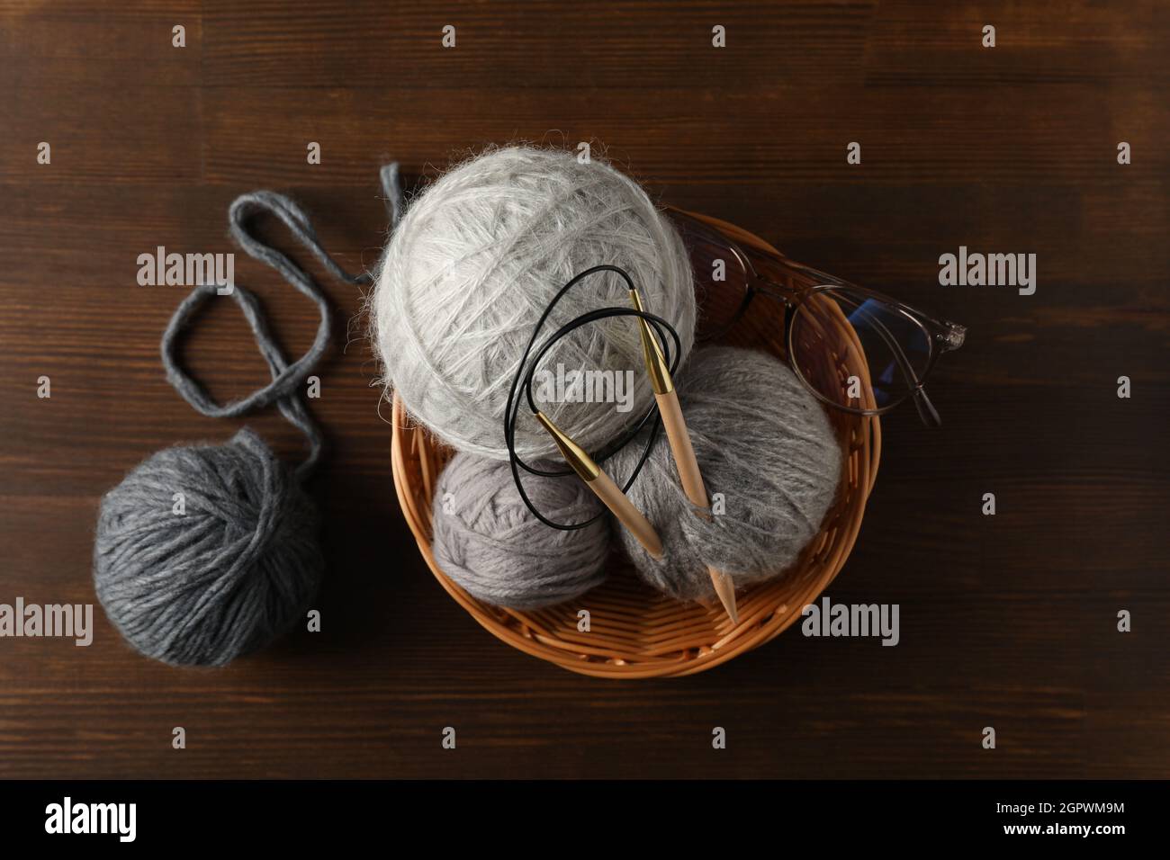 Bol en osier avec boules de fils et aiguilles à tricoter, et des verres sur fond de bois Banque D'Images