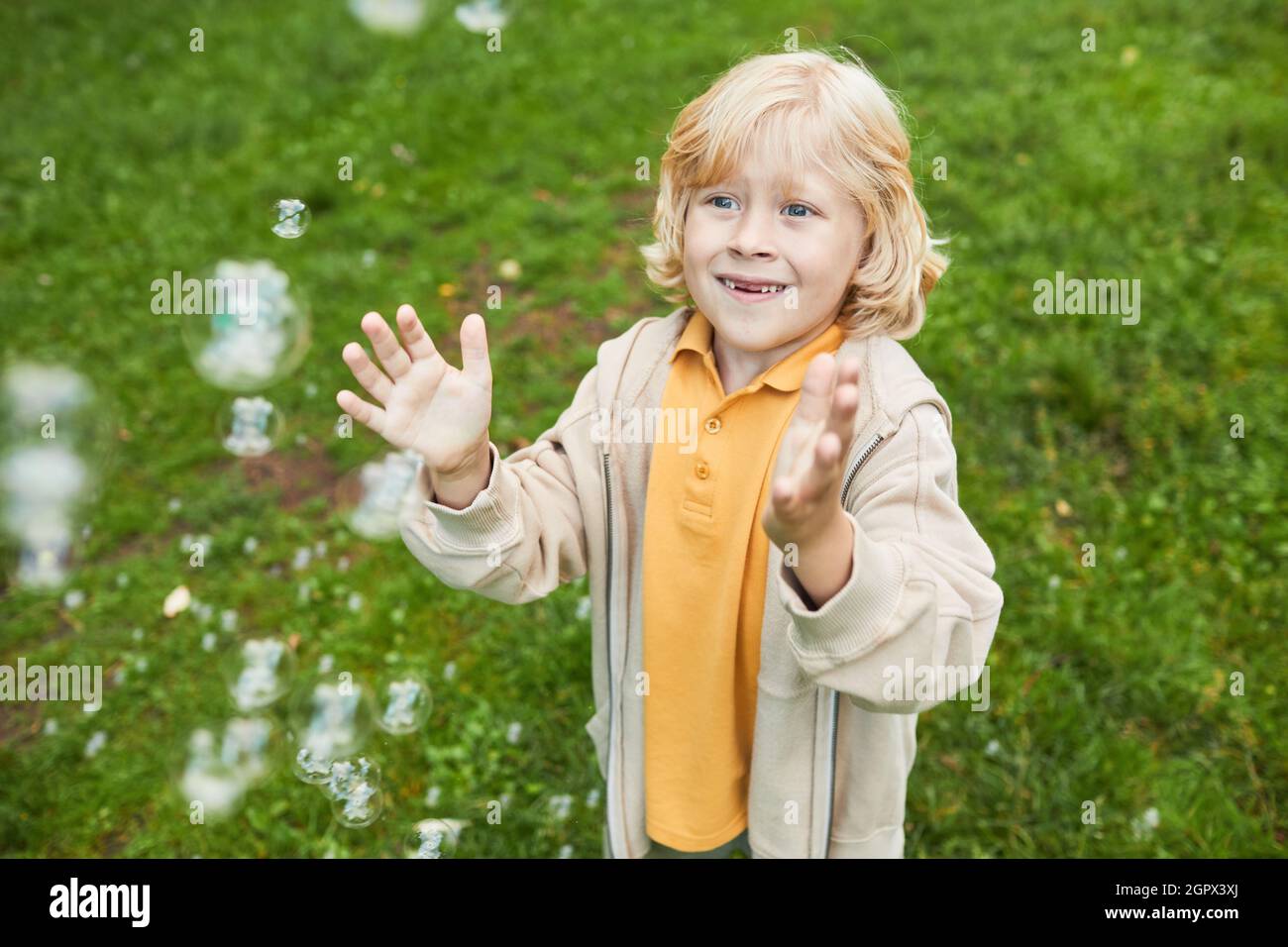 Portrait d'un joli garçon blond jouant avec des bulles à l'extérieur dans le parc et souriant, espace de copie Banque D'Images