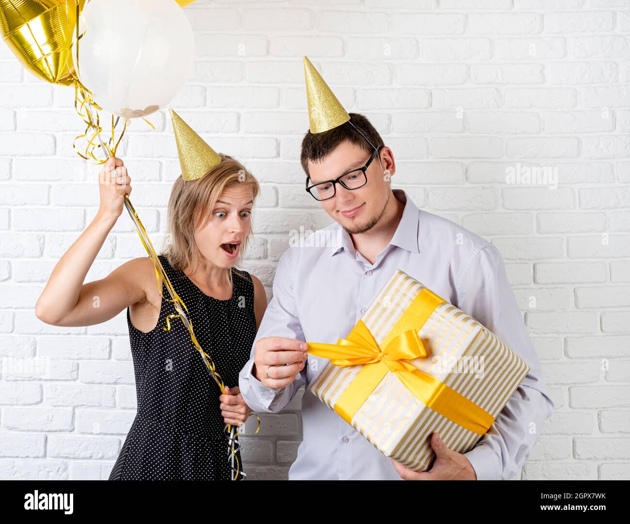 Drole Jeune Couple Celebrant Anniversaire Ouverture Grande Boite Cadeau Sur Fond De Brique Blanche Photo Stock Alamy